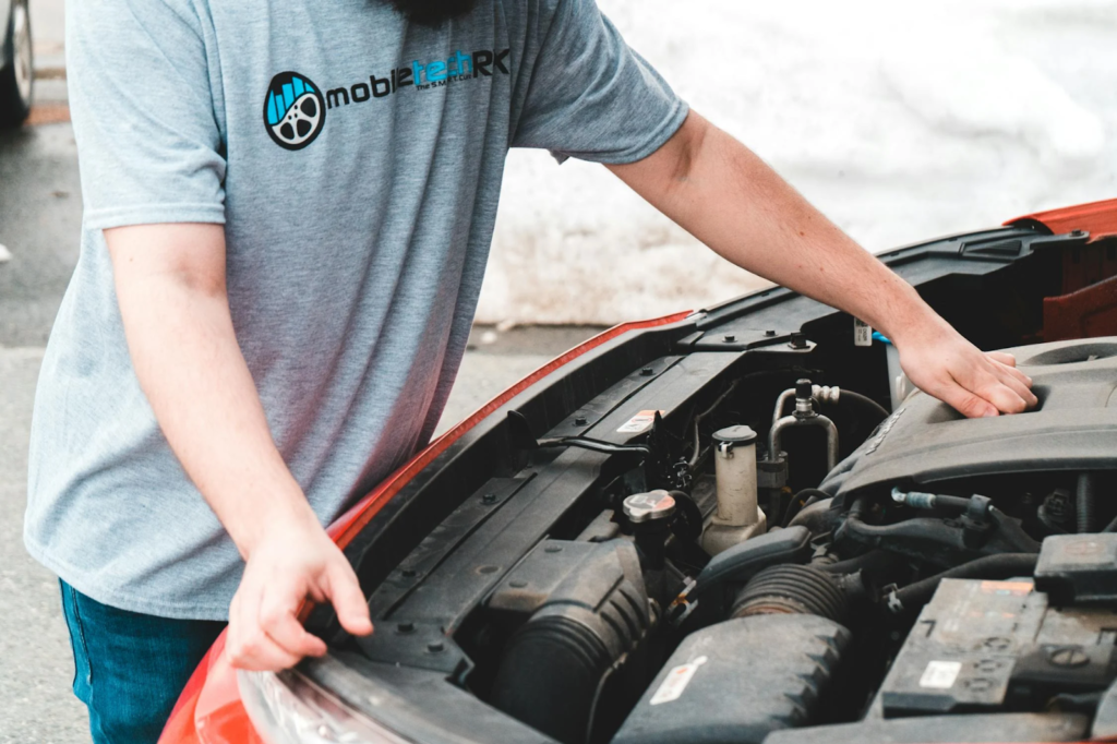 Man inspecting the engine compartment of a red car with the hood open.